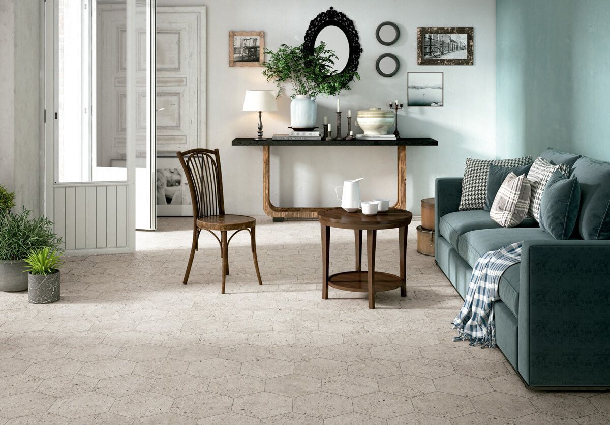 Sala de estar con sofá azul, mesa de madera, espejo ornamentado y suelo de terrazo de color claro.