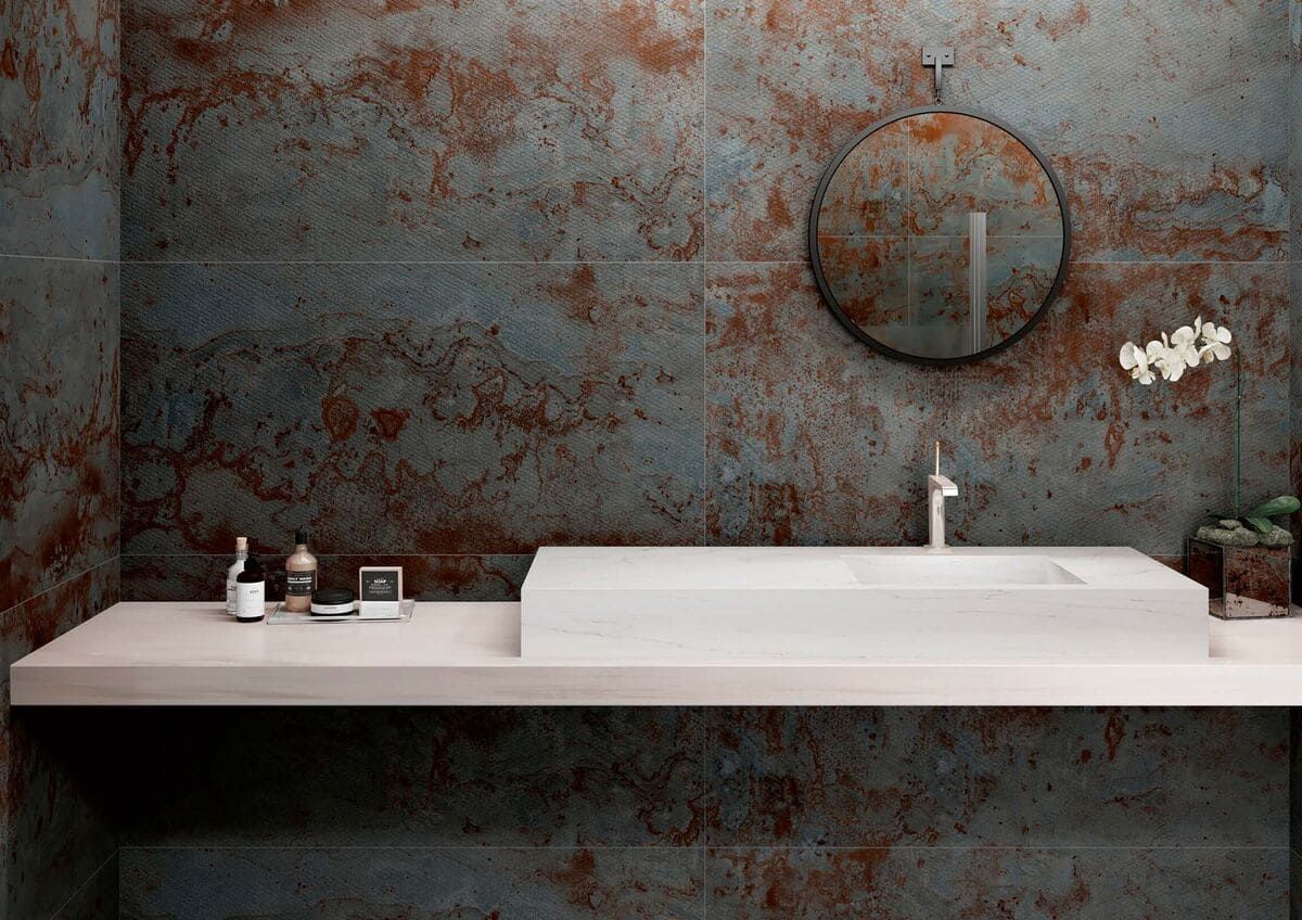 Baño moderno con paredes texturizadas de color óxido, lavabo flotante blanco y espejo redondo.