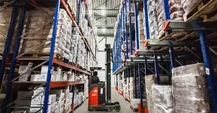 Empilhadeira em um armazém com prateleiras altas repletas de mercadorias.