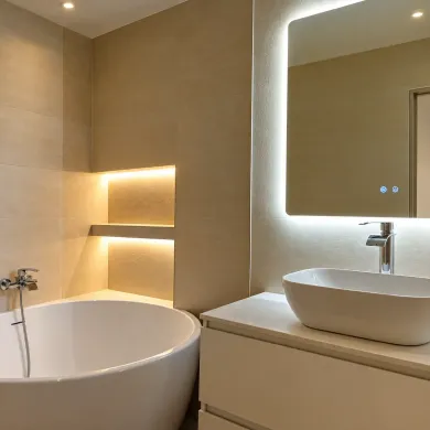Baño moderno con bañera independiente, nichos de pared iluminados y lavabo con espejo iluminado.