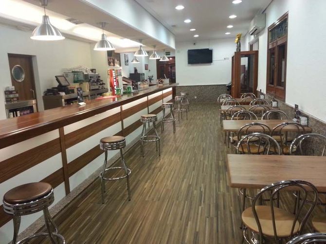 Bar y comedor vacíos con taburetes, mesas y suelo de madera, vistos desde la entrada.