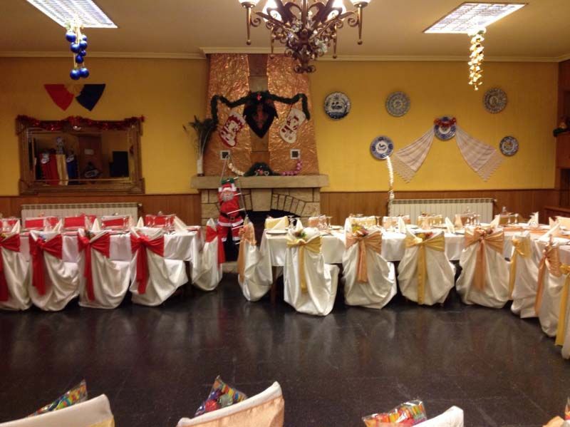 Salón de banquetes decorado con fundas de sillas rojas y blancas, candelabros y decoración festiva en las paredes.