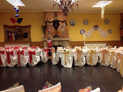 Salón de banquetes decorado con fundas de sillas rojas y blancas, candelabros y decoración festiva en las paredes.