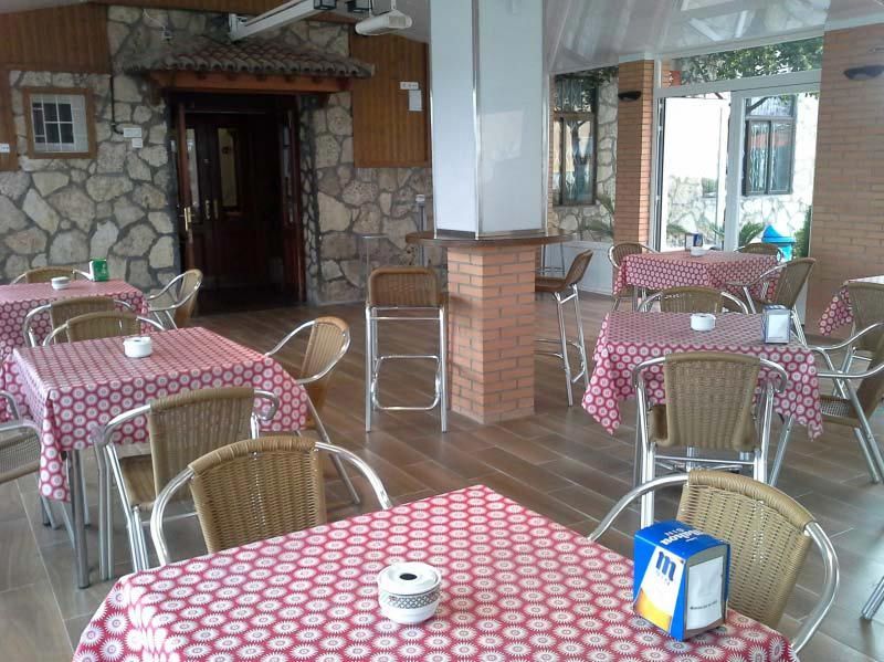 Cafetería al aire libre con manteles de cuadros rojos y sillas de mimbre en un patio cubierto.