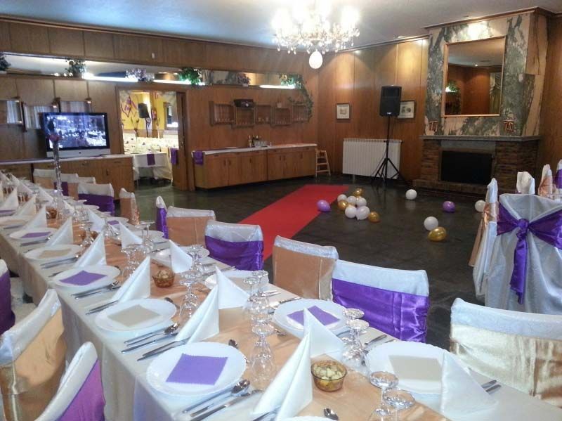 Salón de banquetes decorado con mesas en blanco y morado y un pasillo con alfombra roja.