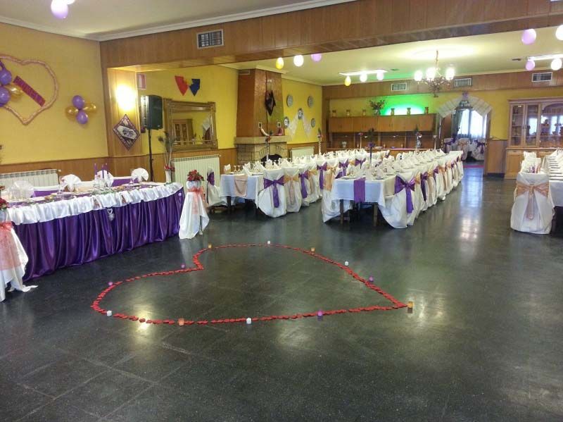 Salón de banquetes decorado con mesas largas, manteles morados y luces en forma de corazón en el suelo.