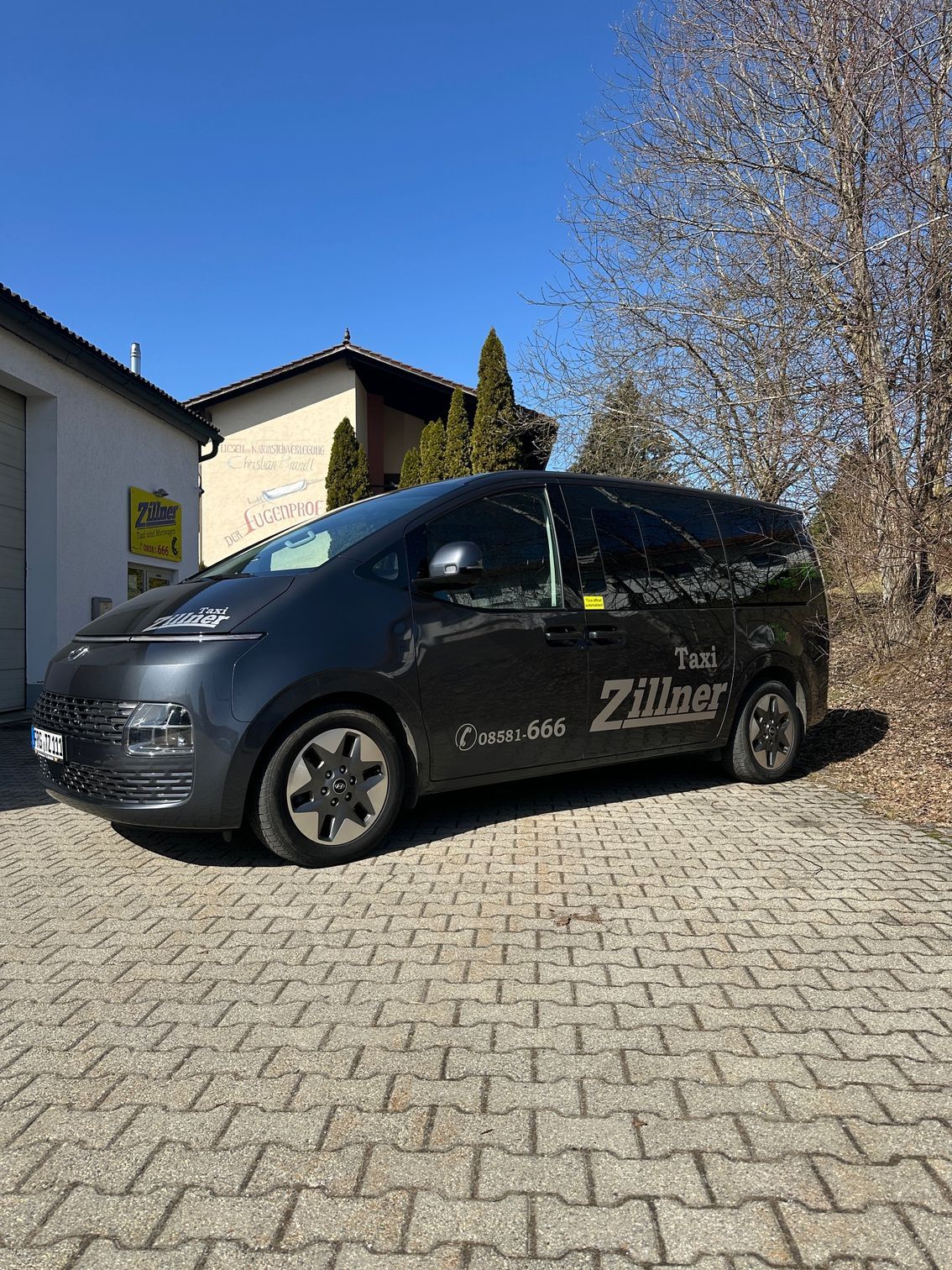 Ein dunkles Taxi von der Seite vor dem markanten weißen Gebäude der Taxizentrale aufgenommen