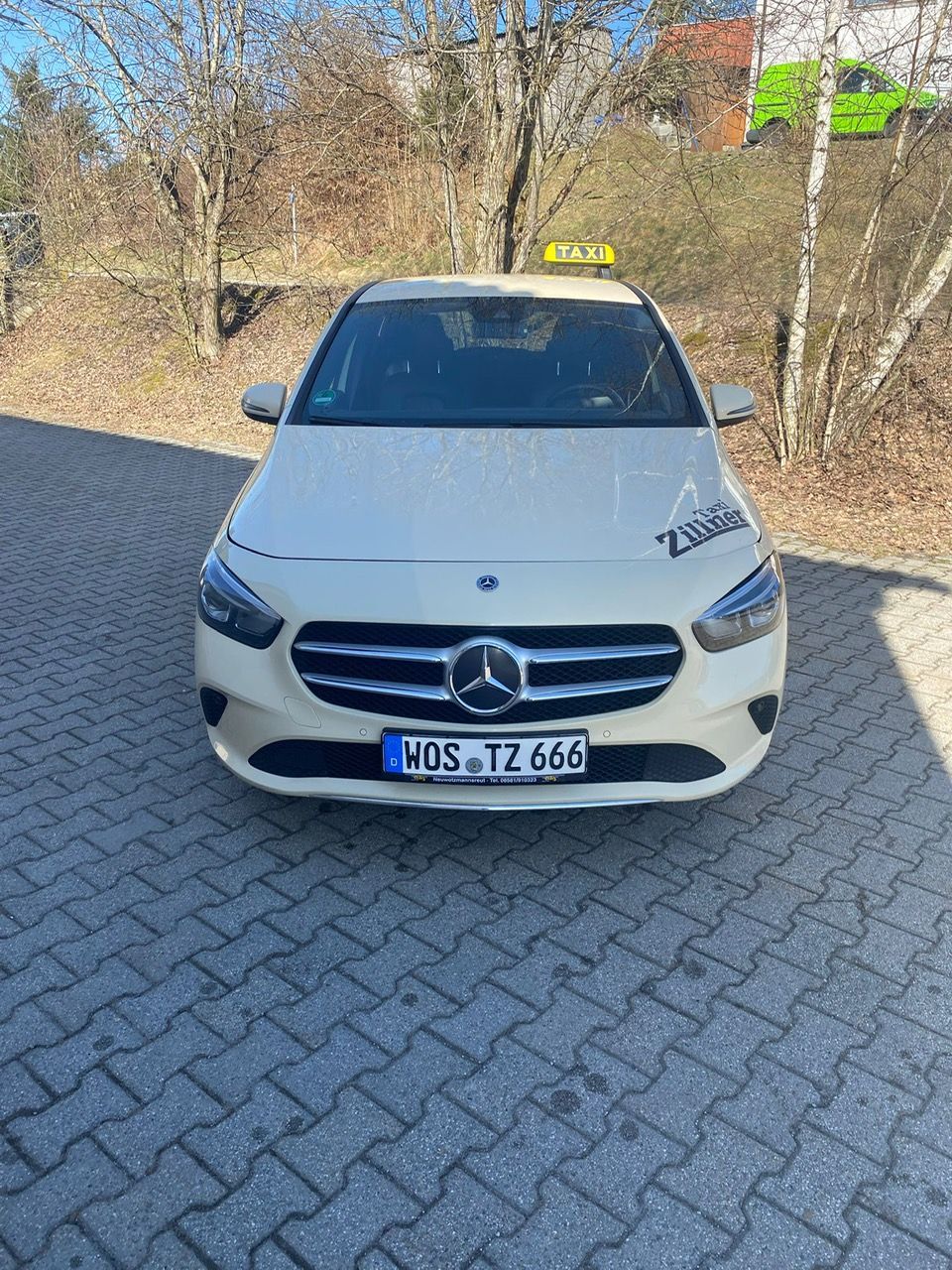 Frontale Ansicht eines hellen Taxis mit gelbem Taxischild auf dem Parkplatz.