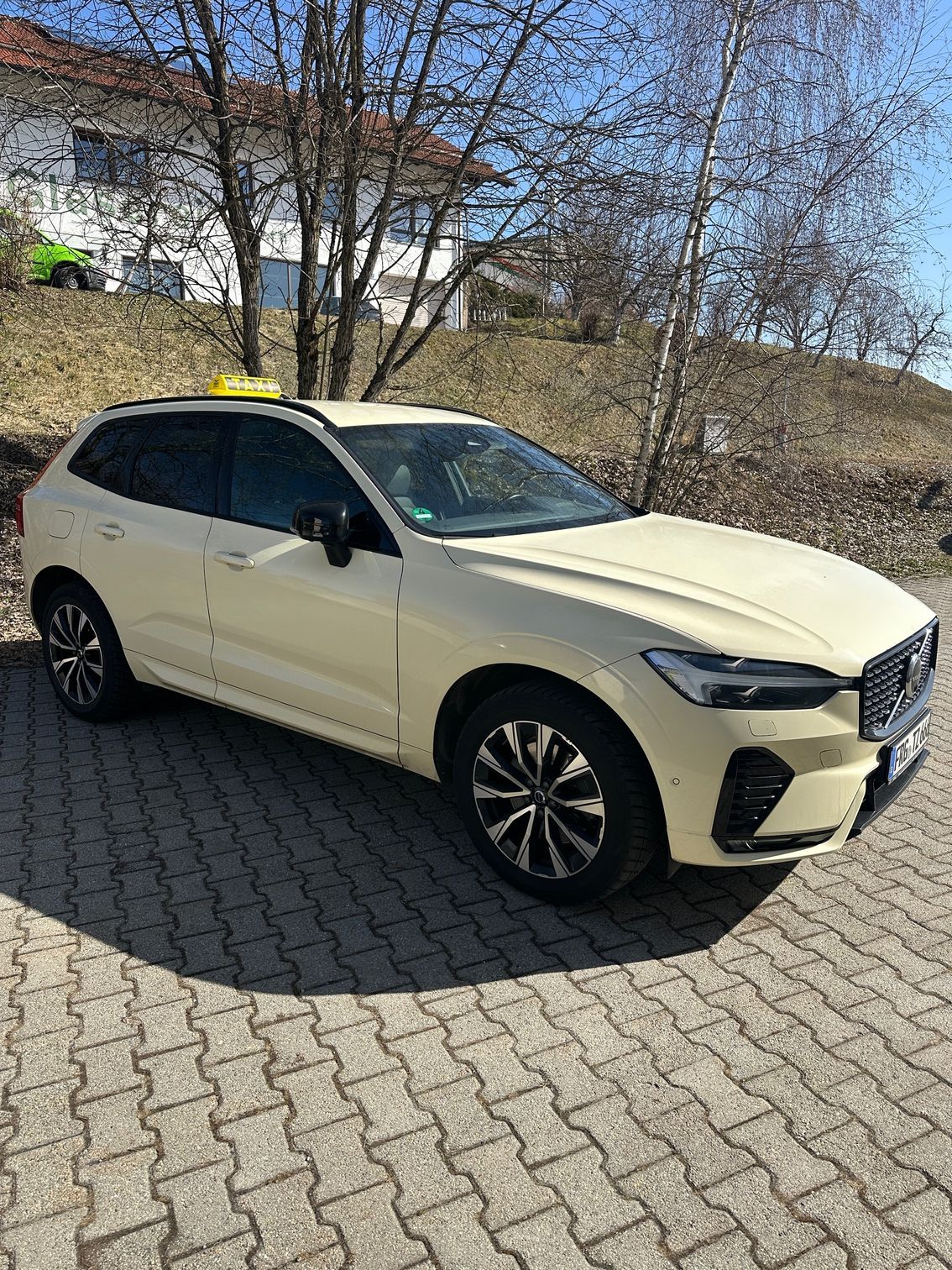 Seitenprofil eines hellen Taxis (Kombi) vor einem Wohnhaus und kahlen Bäumen.