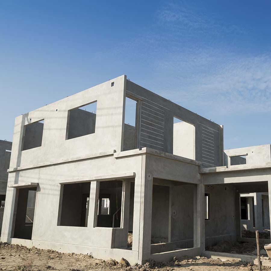 Casa de hormigón de dos pisos en construcción contra un cielo azul, con paredes y aberturas de ventanas sin terminar.