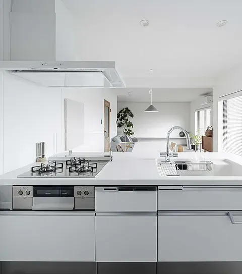 Cocina moderna, blanca y luminosa con placa de cocina, fregadero y decoración minimalista. Vista a la sala de estar.