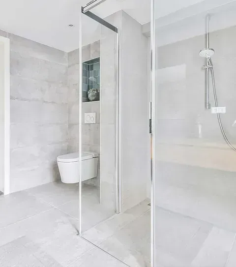 Baño moderno y minimalista con azulejos grises y mampara de ducha de cristal. Inodoro flotante.