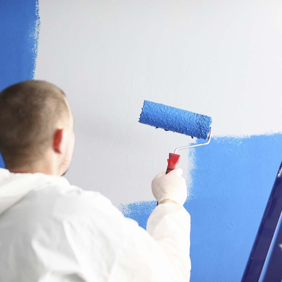 Hombre con traje de protección pintando una pared de color azul con un rodillo de pintura.