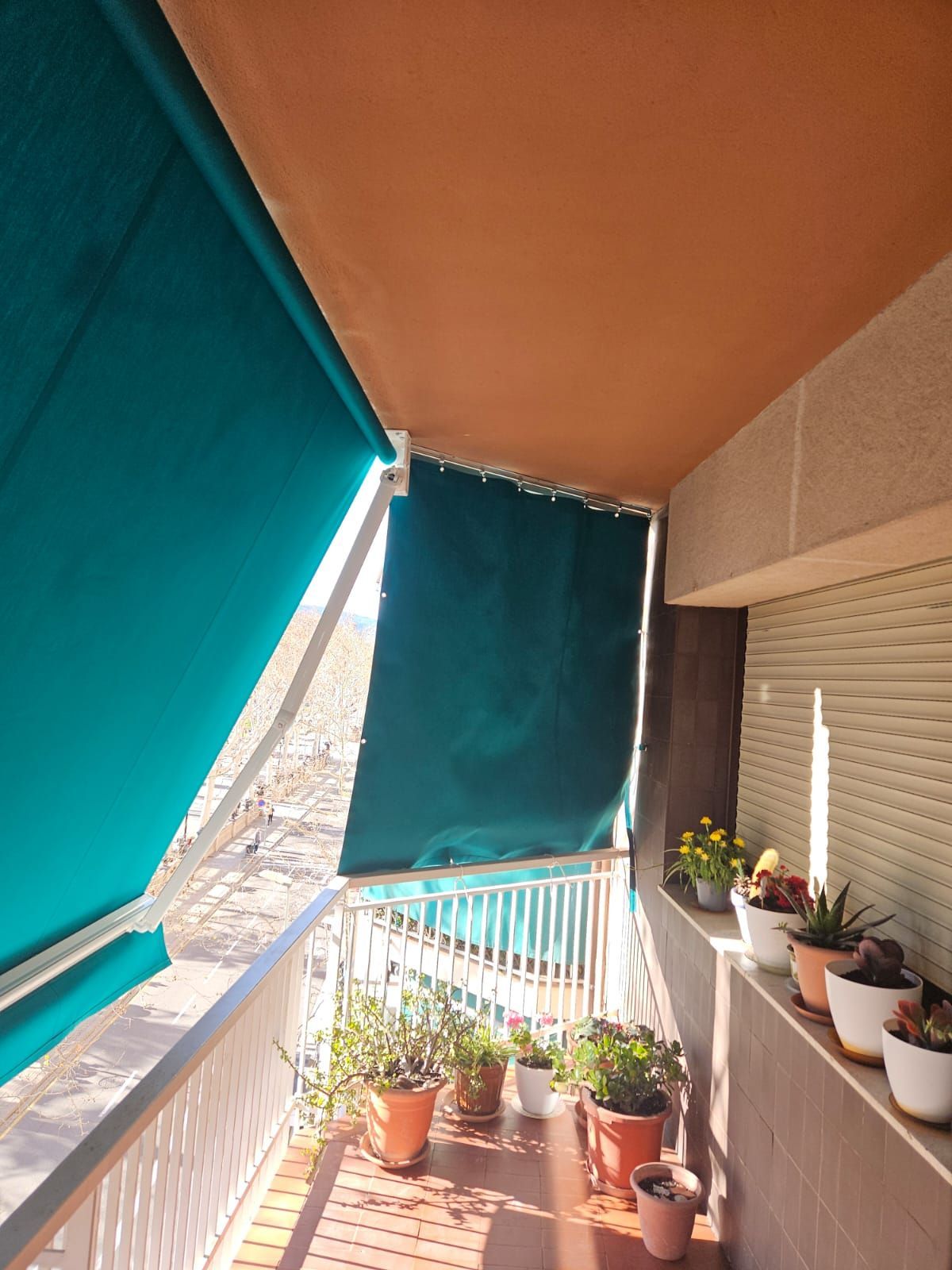 Un balcón con un toldo verde y plantas en macetas.