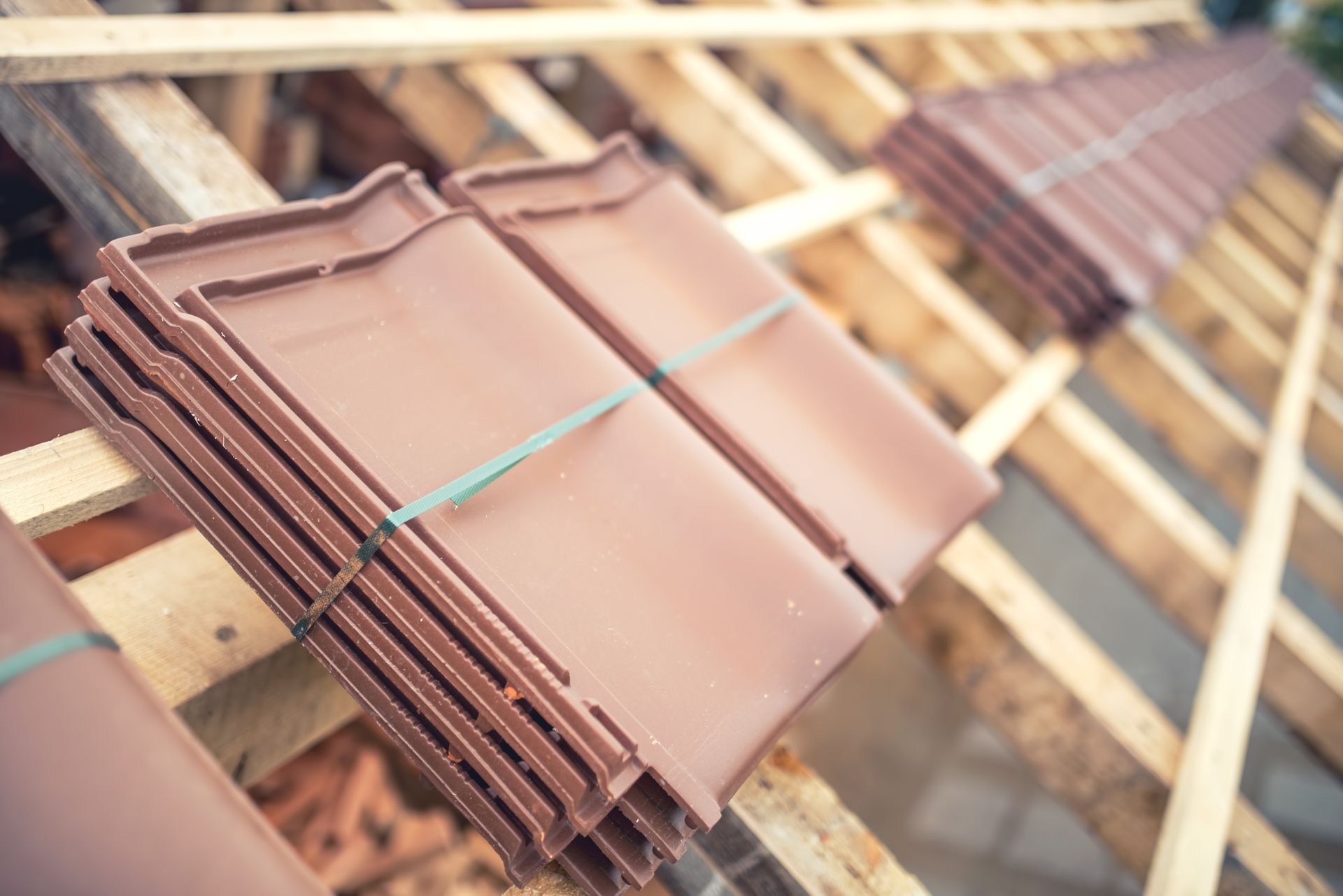Piles de tuiles en terre cuite sur une charpente de toit en bois, prêtes à être installées.