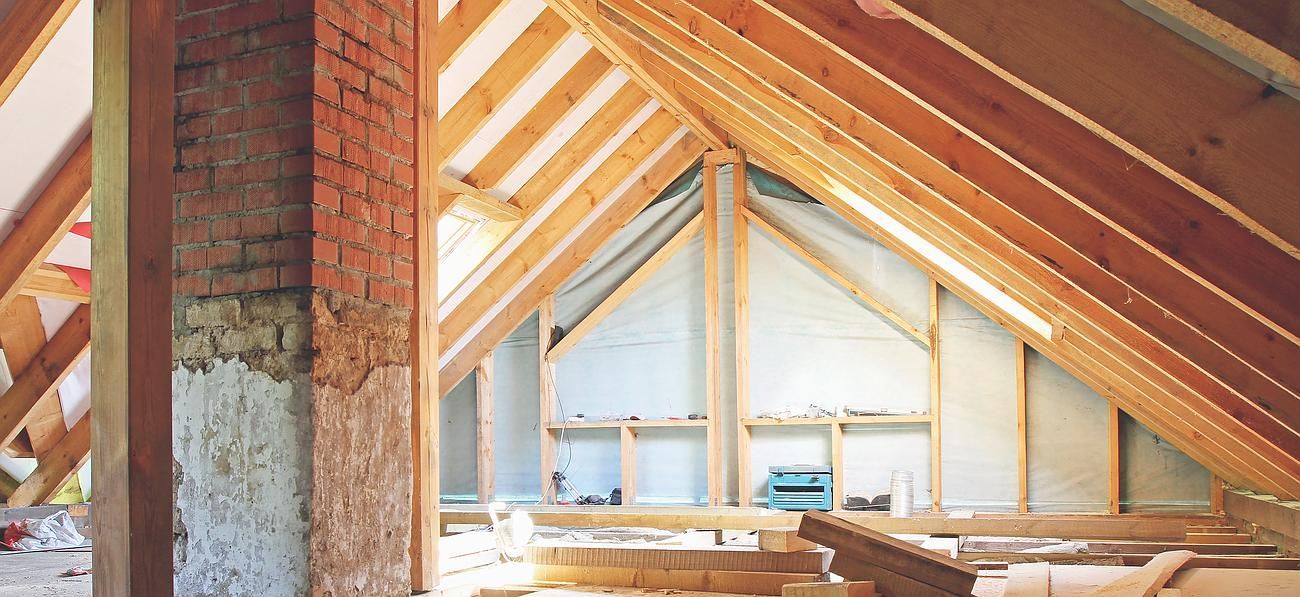 Intérieur d'un grenier en construction avec poutres en bois apparentes, briques et isolation.