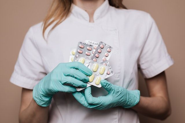 Una enfermera que lleva guantes verdes sostiene un blíster de pastillas.
