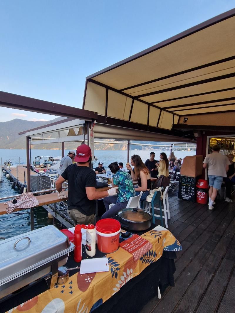 Un gruppo di persone è seduto ai tavoli di un ristorante che si affaccia su uno specchio d'acqua.