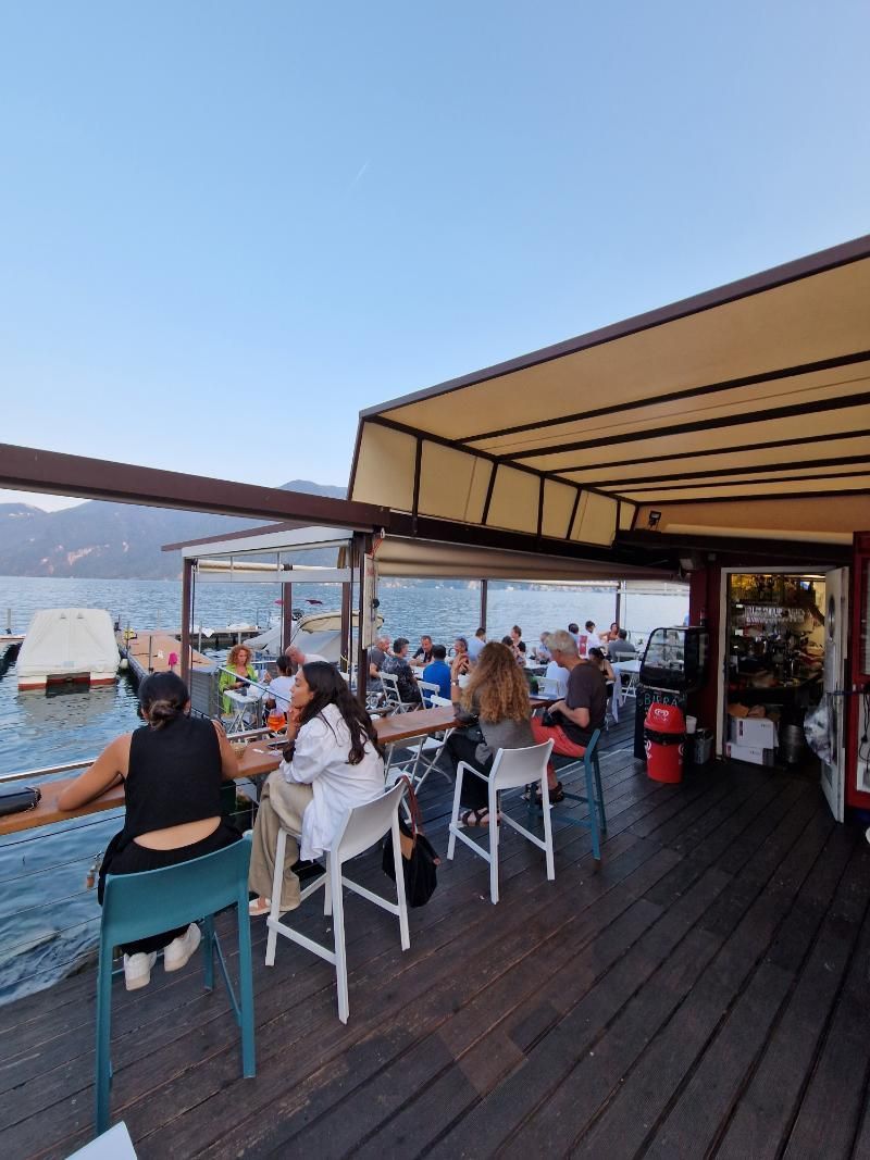 Un gruppo di persone è seduto ai tavoli su un ponte che si affaccia sull'acqua.