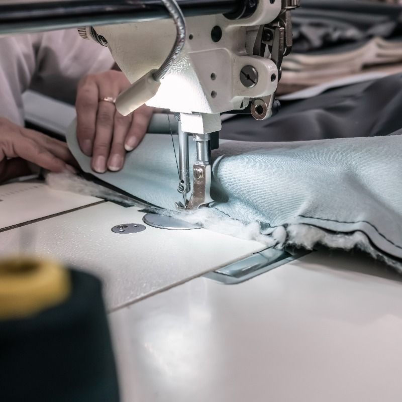 Primer plano de una máquina de coser cosiendo tela azul claro mientras unas manos guían el material.