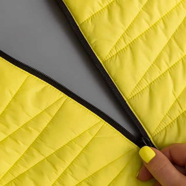 Una mano sujeta una cremallera negra en una chaqueta acolchada de color amarillo brillante.