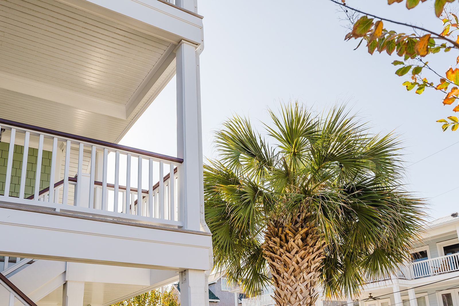 A white house with a balcony and a palm tree in front of it.