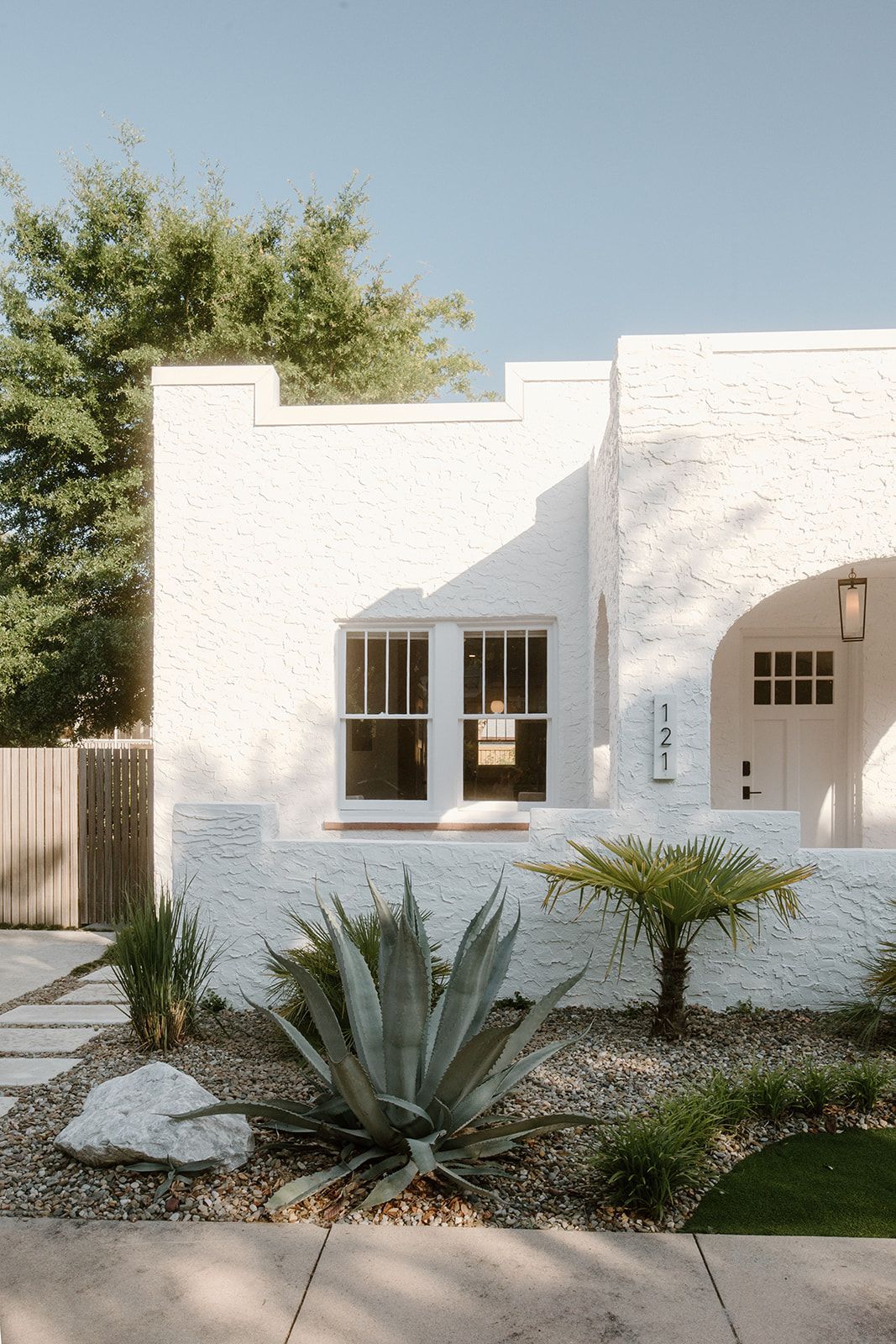 A white house with a lot of windows and plants in front of it.