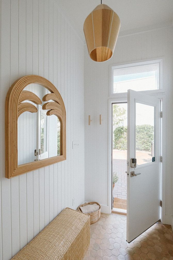 A hallway with a bench , mirror and door.