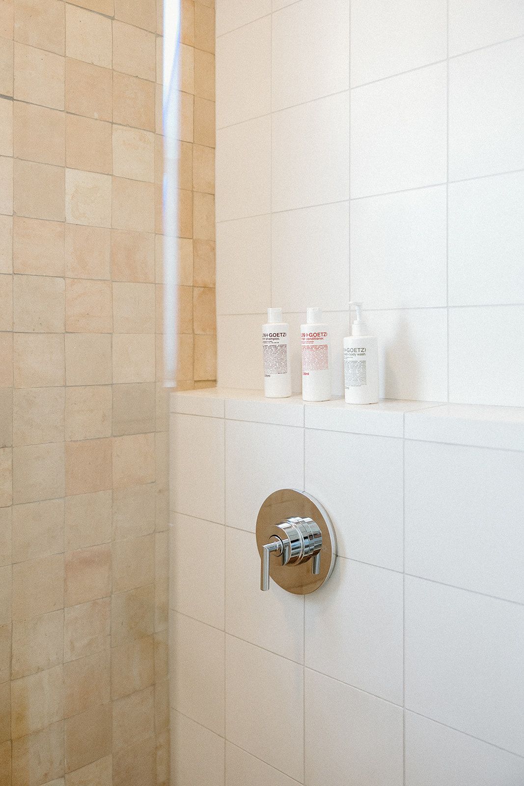 A bathroom with a shower and a shelf with bottles on it.  The Sunsetter