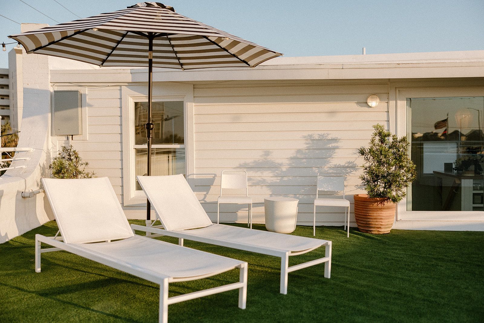 There are two lounge chairs and an umbrella on the roof of a house.