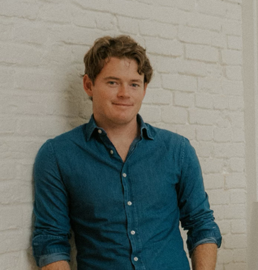 A man in a blue shirt is leaning against a white brick wall