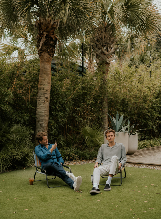 Two men are sitting in chairs on a lush green lawn.