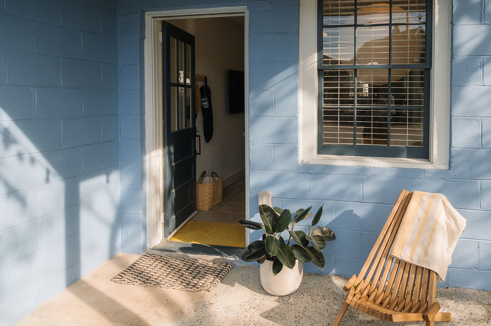 A blue brick house with a chair and a potted plant on the porch.