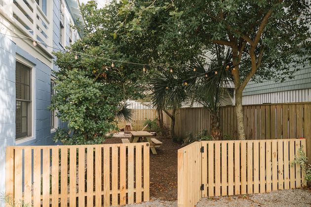 A wooden fence surrounds a backyard with a picnic table and trees.