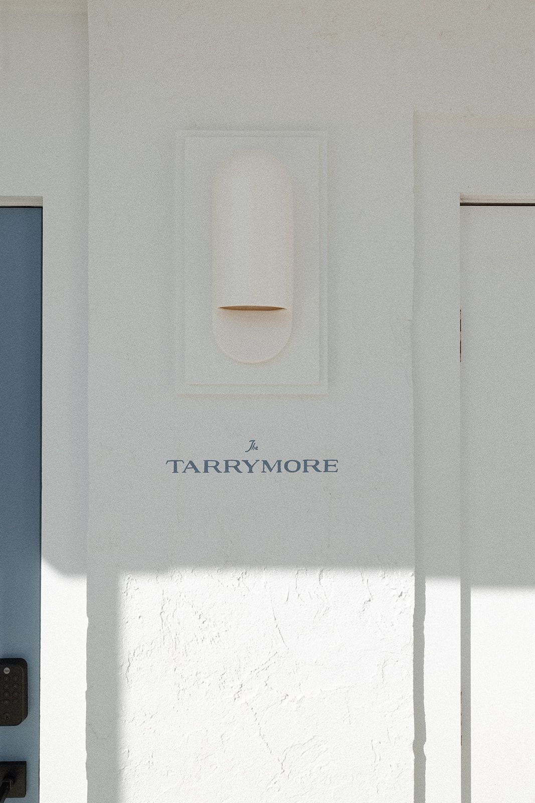 A white wall with a blue door and a light on it.