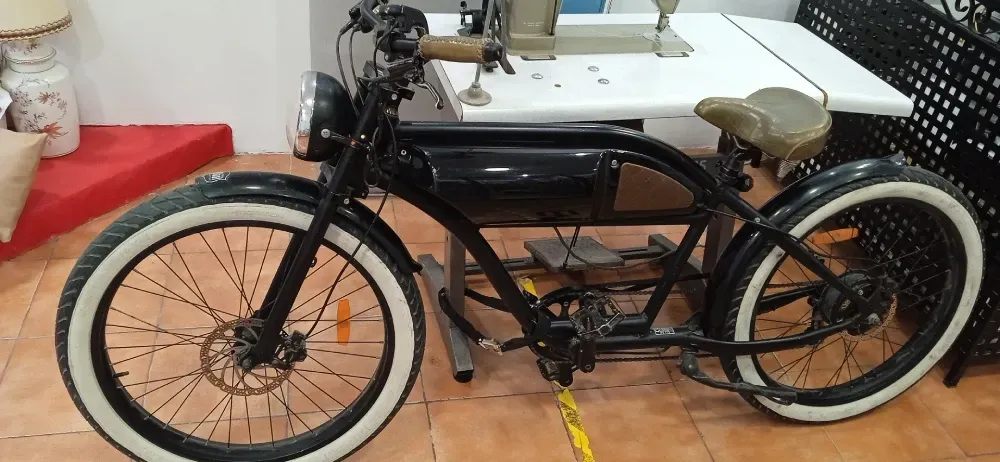 Una bicicleta negra con neumáticos blancos está estacionada frente a una máquina de coser.