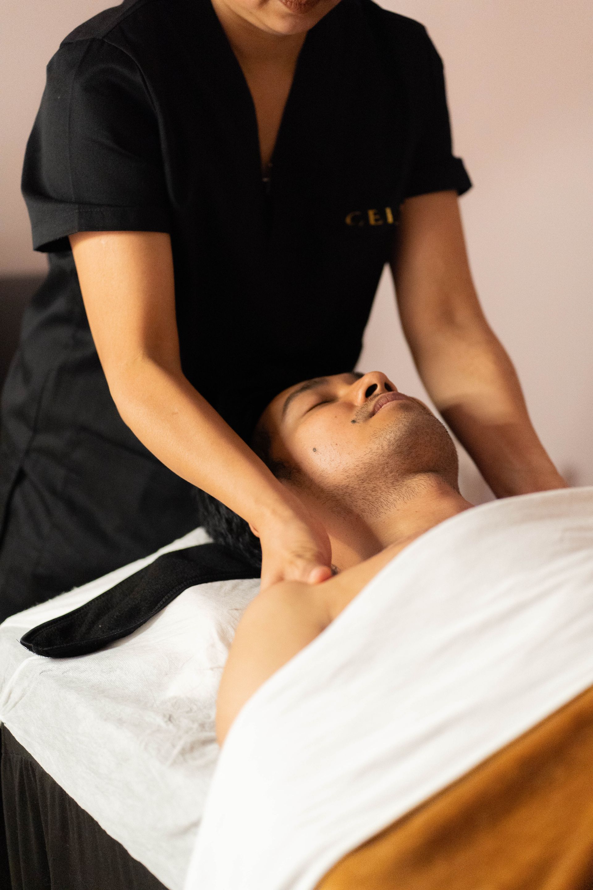 Un masajista realiza un masaje de hombros a una persona que yace sobre una camilla de masaje.