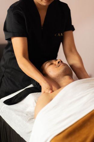 Un masajista realiza un masaje de hombros a una persona que yace sobre una camilla de masaje.