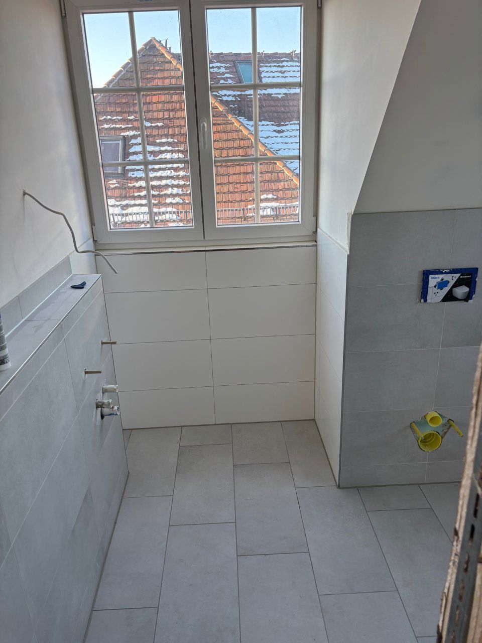 Kleines, gefliestes Badezimmer mit Fenster, weißen Wänden und Duschbereich.