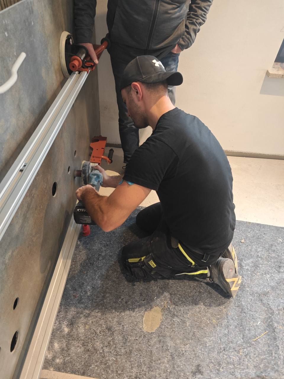 Ein Techniker kniet und montiert mit einem Elektrowerkzeug Beschläge an einer Wandplatte.