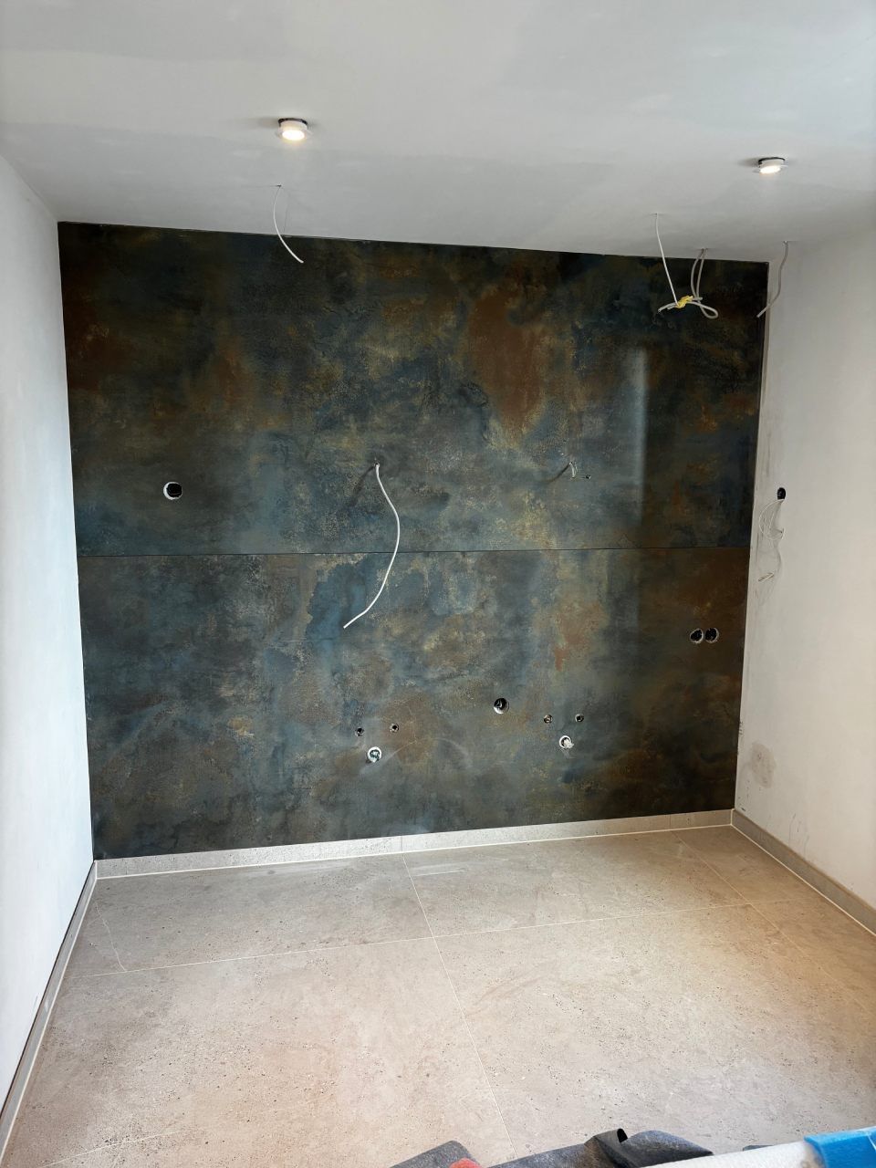 Leerer Raum mit weißen Wänden, Teppichboden und einer dunklen, strukturierten Akzentwand mit sichtbaren Löchern.