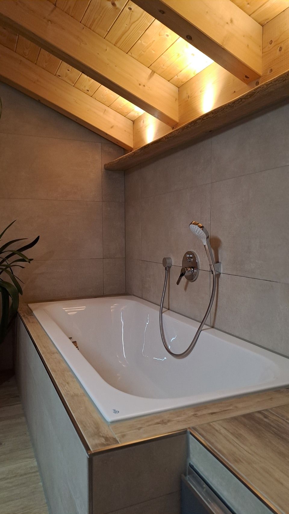 Eckbadewanne unter einer schrägen Holzdecke mit Handbrause und holzverkleideter Umrandung