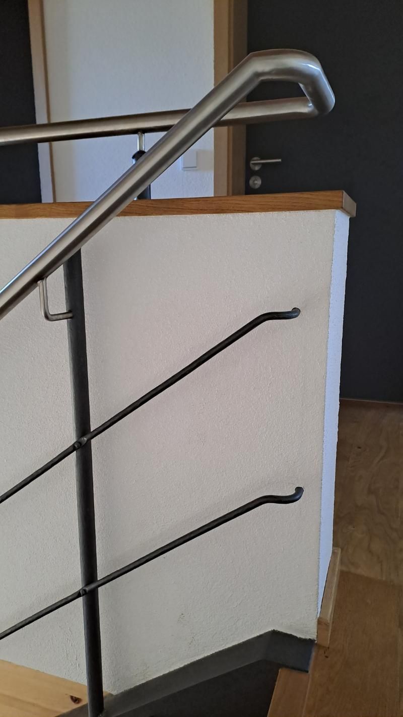 Über einer weißen Wand schwingt sich ein Handlauf aus Edelstahl, an dem zwei dünne, schwarze