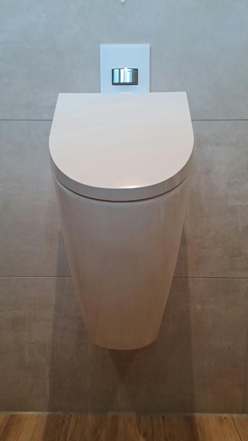 Ein wandmontiertes, cremefarbenes Keramikurinal mit einem Spülknopf