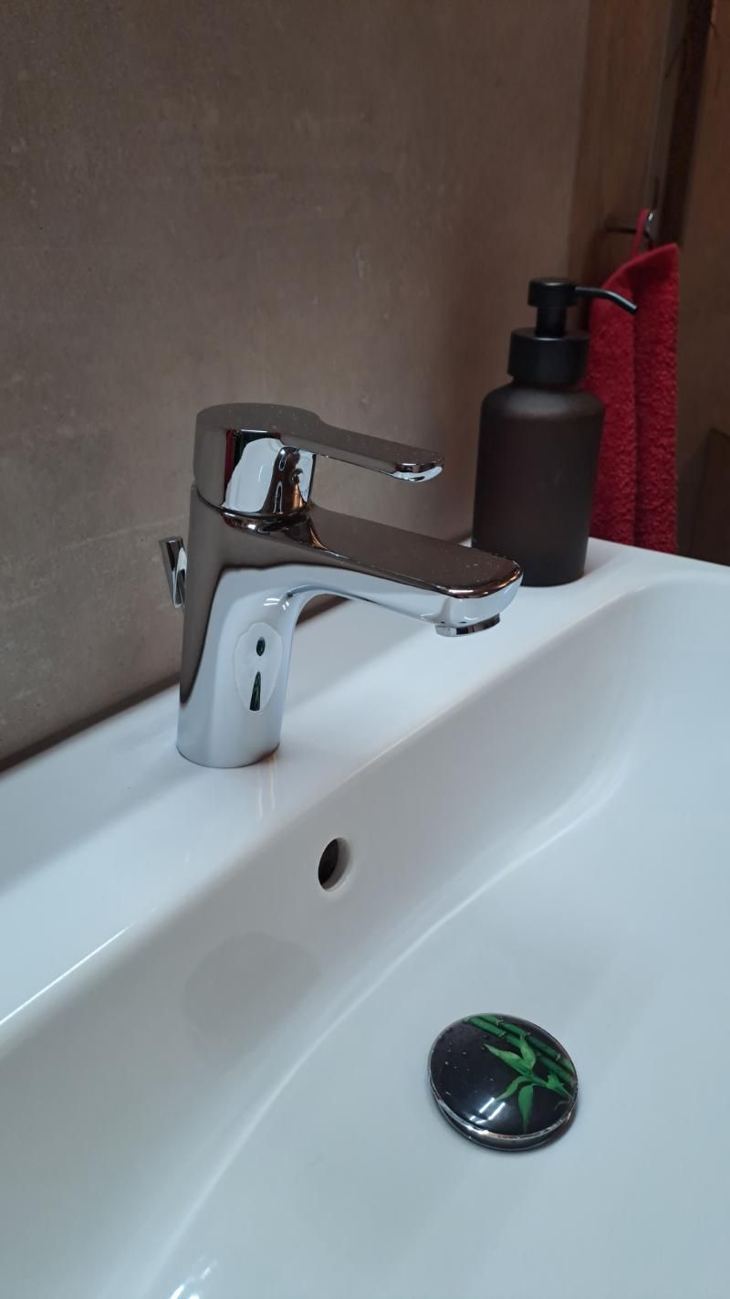 Ein moderner, verchromter Badezimmerhahn auf einem weißen Porzellanwaschbecken mit dunklem Seifenspender 