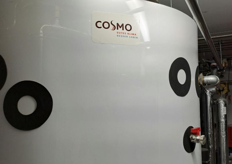 Ein weißer Industrietank der Marke Cosmo mit schwarzen kreisförmigen Markierungen und einem Ventil mit rotem Griff