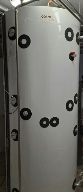 Grauer Industrietank mit schwarzen Armaturen und einem roten Ventil in einer Fabrikumgebung