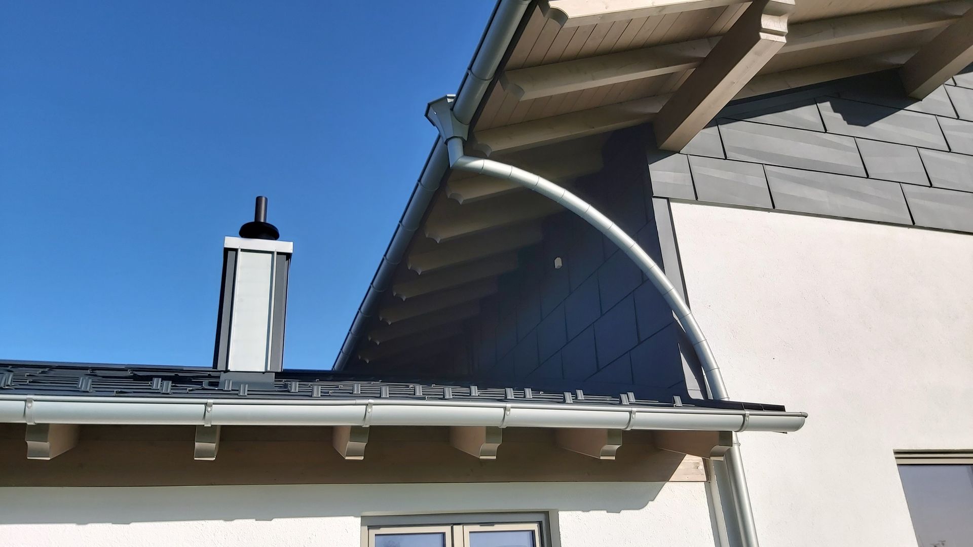 Ein zweistöckiges Haus mit grauer Garage und Solarpaneelen auf dem Ziegeldach unter klarem, blauem Himmel.