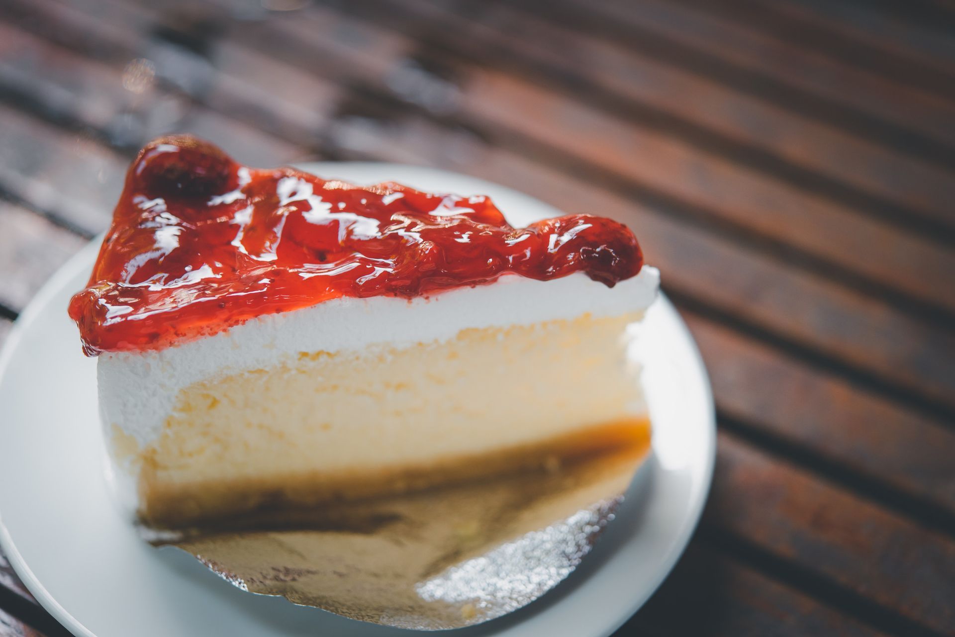 Una rebanada de tarta de queso con fresas en un plato blanco sobre una mesa de madera.