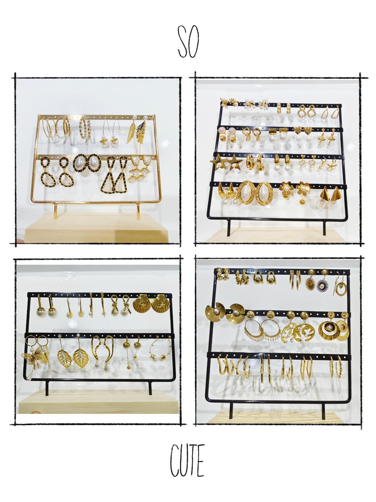 Cuatro expositores con aretes dorados sobre soportes negros con bases de madera, dentro de un expositor con marco blanco. La inscripción 